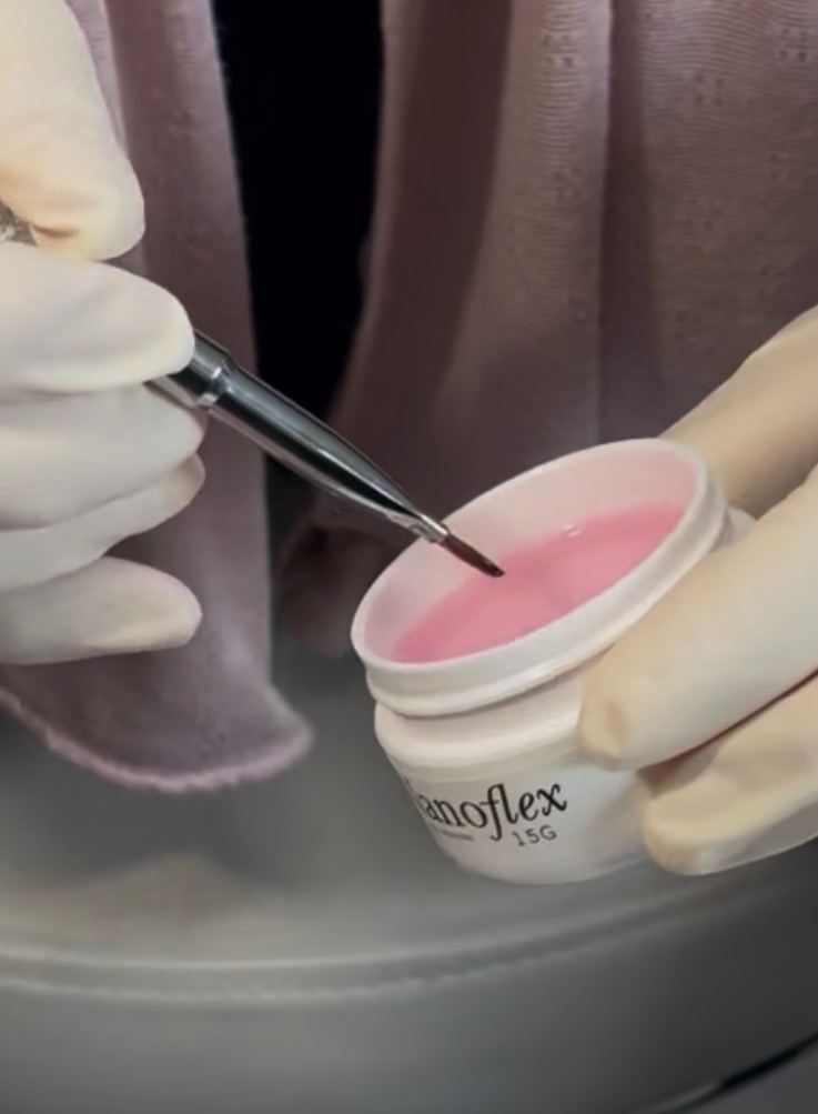Gloved hands loading NanoFlex reconstruction gel onto a brush at Shifa Nail Care